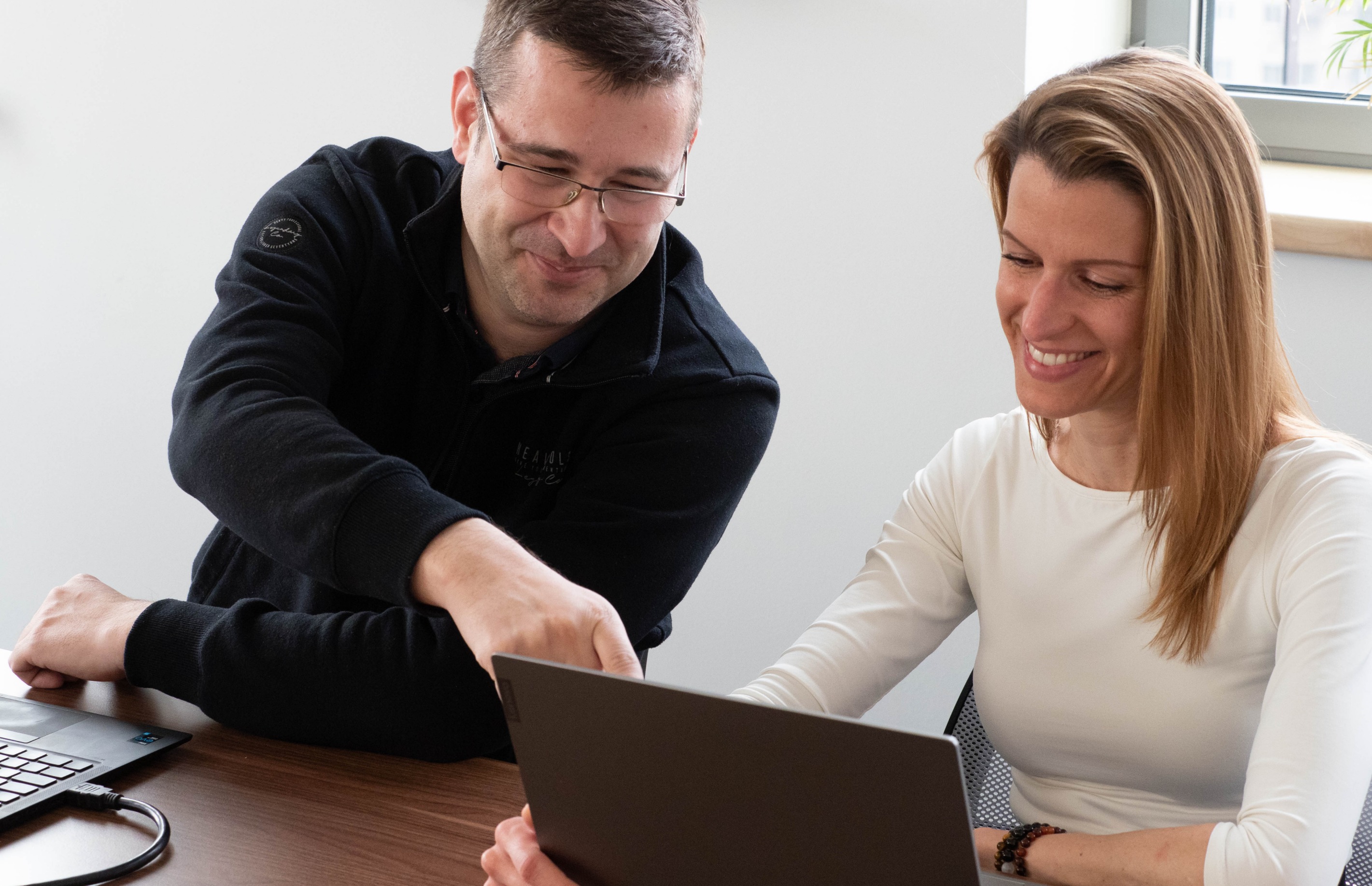 Two coworkers sitting in front of a laptop discussing work.